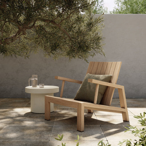 Wooden outdoor lounge chair with a pillow on a patio with a small table and plants.